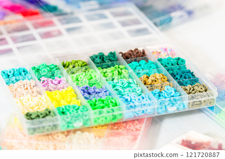 Assorted clay bead boxes neatly arranged on a white table, awaiting a creative kids' craft project. 121720887