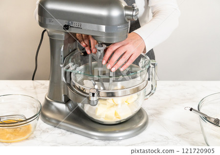 Front view of an electric stand mixer in use, blending ingredients for Classic Sugar Cookie Dough. The baker hands are steadying the bowl as the mixer combines butter, sugar, and other ingredients on Front view of an electric stand mixer in use, blending ingredients for Classic Sugar Cookie Dough. The baker hands are steadying the bowl as the mixer combines butter, sugar, and other ingredients on 121720905