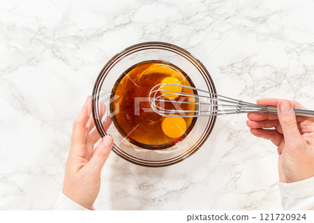 Overhead view of a bowl with wet ingredients including two eggs and maple syrup for Pale Gingerbread Cookies with Subtle Spice Flavor. The rich, amber maple syrup contrasts with the bright yellow of 121720924