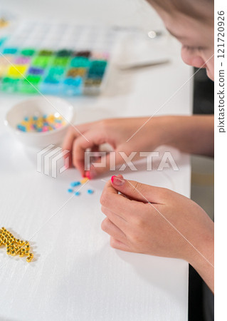 Little girl enjoys crafting colorful bracelets with vibrant clay beads set. 121720926