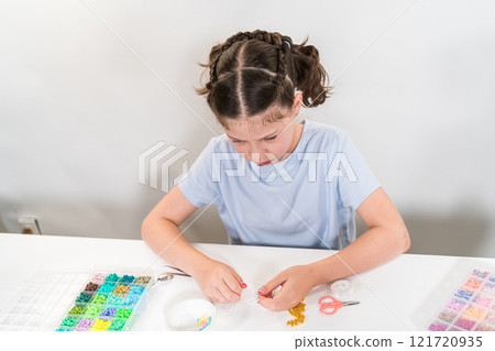 Little girl enjoys crafting colorful bracelets with vibrant clay beads set. 121720935