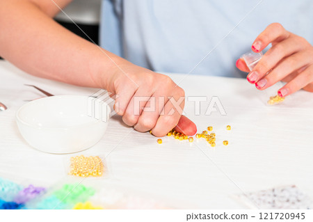 Little girl enjoys crafting colorful bracelets with vibrant clay beads set. 121720945