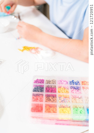 Little girl enjoys crafting colorful bracelets with vibrant clay beads set. 121720951