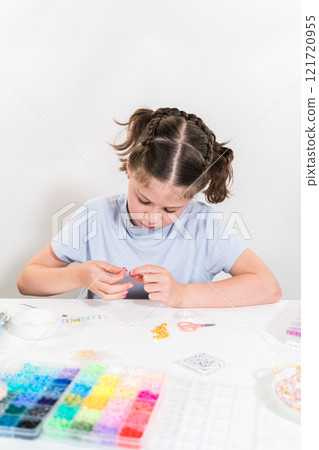 Little girl enjoys crafting colorful bracelets with vibrant clay beads set. Little girl enjoys crafting colorful bracelets with vibrant clay beads set. 121720955