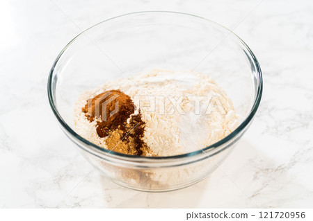 Close-up view of a large glass mixing bowl with flour and a measured amount of spices (including cinnamon and ginger) added on top, ready to be mixed for the Amber Gingerbread Cookie Dough. Close-up view of a large glass mixing bowl with flour and a measured amount of spices (including cinnamon and ginger) added on top, ready to be mixed for the Amber Gingerbread Cookie Dough. 121720956