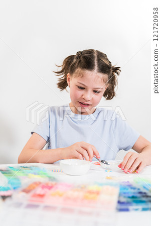 Little girl enjoys crafting colorful bracelets with vibrant clay beads set. Little girl enjoys crafting colorful bracelets with vibrant clay beads set. 121720958