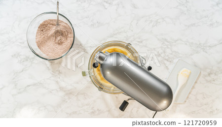 Overhead view of a stand mixer with Chocolate Ginger Sugar Cookie Dough ingredients, showcasing the setup of dry and wet ingredients on a marble countertop. 121720959