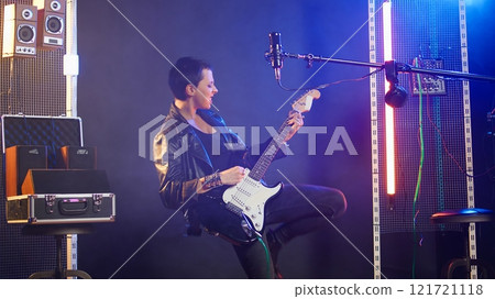 Female recording artist playing bass guitar in a nightclub concert, wearing a leather jacket and performing live with edgy bold attitude. Heavy metal musical talent in the studio. Camera A. Female recording artist playing bass guitar in a nightclub concert, wearing a leather jacket and performing live with edgy bold attitude. Heavy metal musical talent in the studio. Camera A. 121721118