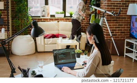 Software developer types programming code in a cozy home office setup. Asian woman coding for cloud computing on her laptop, enhances productivity for software development. Camera A. Software developer types programming code in a cozy home office setup. Asian woman coding for cloud computing on her laptop, enhances productivity for software development. Camera A. 121721177