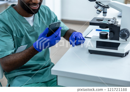 Scientist in laboratory conducting experiment and tests on samples using mobile phone and microscope 121721188
