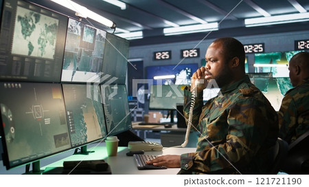 Military soldier in mission command post overseeing national safety operations, talking on phone. African american army expert in telephone call in monitoring room, camera B 121721190