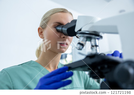 Woman technician in lab looking at samples under microscope for test in pharmaceutical research 121721198