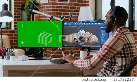 Software developer creates a gear prototype on dual monitors next to chroma key display, home office remote work. Expert does 3D modeling for innovation in the industrial design industry. Camera B. Software developer creates a gear prototype on dual monitors next to chroma key display, home office remote work. Expert does 3D modeling for innovation in the industrial design industry. Camera B. 121721237