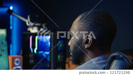 Man at home plays online multiplayer spaceship videogame with friends, relaxing, close up. African american player, flying spacecraft, enjoying leisure time in RGB lights adorn apartment, camera B 121721298