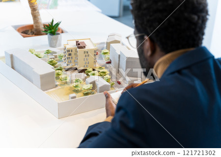 African american young architect sitting at the table and analyzing new model 121721302