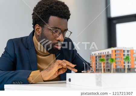 African american young architect sitting at the table and analyzing new model African american young architect sitting at the table and analyzing new model 121721307