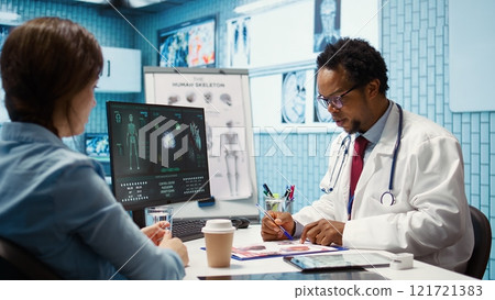 Male physician doing an x ray diagnostics scan interpretation during check up visit, discussing about recovery treatment in cabinet. Doctor examining radiography test results for a patient. Camera B. Male physician doing an x ray diagnostics scan interpretation during check up visit, discussing about recovery treatment in cabinet. Doctor examining radiography test results for a patient. Camera B. 121721383