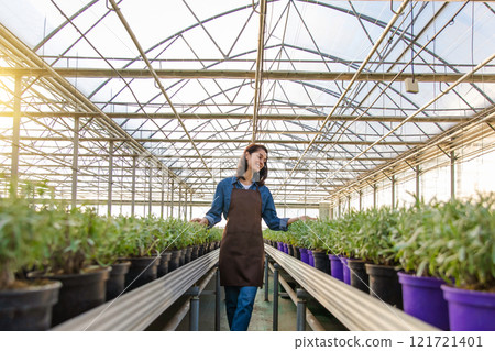 Pretty caucasian young woman standing in a greenhouse near the plants Pretty caucasian young woman standing in a greenhouse near the plants 121721401