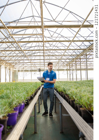 Caucasian young man working in a glasshouse and looking involved 121721431