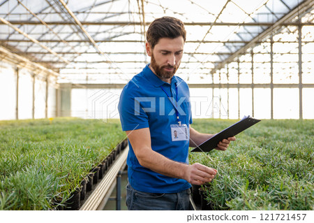 Smiling bearded young caucasian man with a potted plants in hands in a greenhouse 121721457
