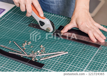 Tanners hands cut leather on a green cutting mat, close-up, process. 121724365
