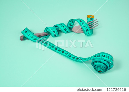 Metal fork and green tape measure on green background Metal fork and green tape measure on green background 121726616