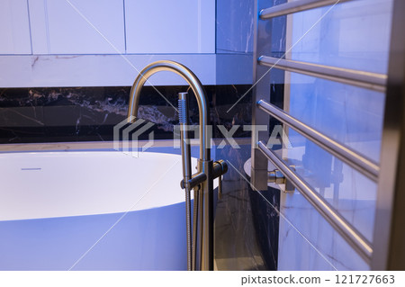 Long stylish Gold faucet on the floor near white bathtub on granite wall background. Modern bathroom interior 121727663