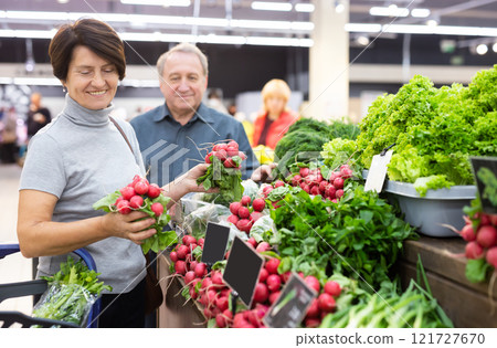 Elderly woman chooses radish in vegetable and fruit department 121727670