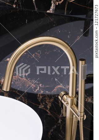 Closeup of gold bathroom faucet next to white bathtub . Gold faucet against a black granite wall Closeup of gold bathroom faucet next to white bathtub . Gold faucet against a black granite wall 121727673