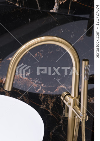 Closeup of gold bathroom faucet next to white bathtub . Gold faucet against a black granite wall Closeup of gold bathroom faucet next to white bathtub . Gold faucet against a black granite wall 121727674