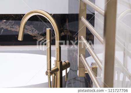Closeup of gold bathroom faucet next to white bathtub . Gold faucet against a black granite wall 121727706