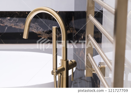 Closeup of gold bathroom faucet next to white bathtub . Gold faucet against a black granite wall Closeup of gold bathroom faucet next to white bathtub . Gold faucet against a black granite wall 121727709