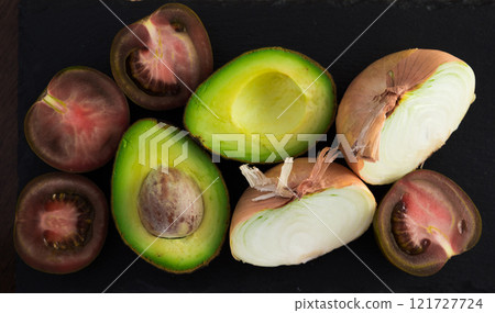 Vegetables black tomatoes, avocado and onions on black stone board Vegetables black tomatoes, avocado and onions on black stone board 121727724