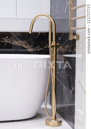 Modern bathroom interior. Exclusive stylish golden faucet on the floor near white bathtub on the background of granite wall. Modern bathroom interior. Exclusive stylish golden faucet on the floor near white bathtub on the background of granite wall. 121727725