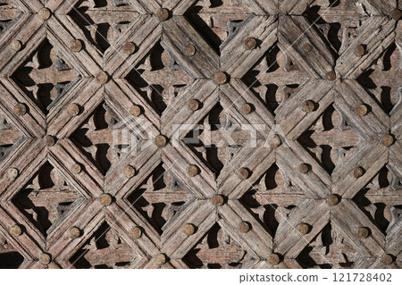 Detailed view of an aged wooden lattice pattern featuring geometric designs and weathered textures, emphasizing artisanal craftsmanship and historical architectural details. 121728402