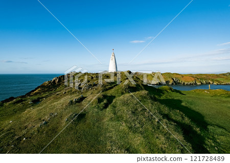Lighthouse stands tall against the blue sky at the rugged coastline on a clear sunny day. Lighthouse stands tall against the blue sky at the rugged coastline on a clear sunny day. 121728489