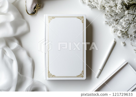 Elegant white book with gilded edges resting on a soft surface beside decorative elements in a serene setting 121729633