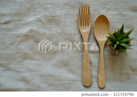 A simple table setting featuring bamboo utensils and a small succulent in a pot on a neutral fabric background 121729796