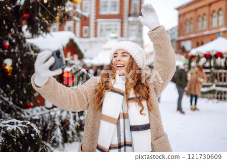 Young tourist uses a smartphone while walking through a Christmas market. 121730609