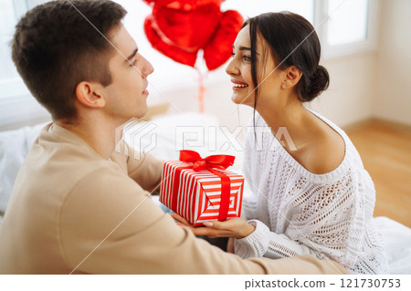 Young couple at home celebrating Valentine's Day. Exchange of gifts. Surprise and love concept. 121730753