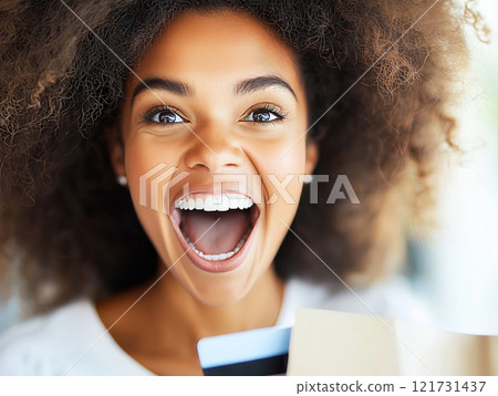 Excited woman with a vibrant smile holding a credit card and a shopping bag, radiating joy 121731437