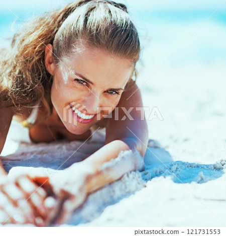 Happy young woman in swimsuit relaxing on beach 121731553