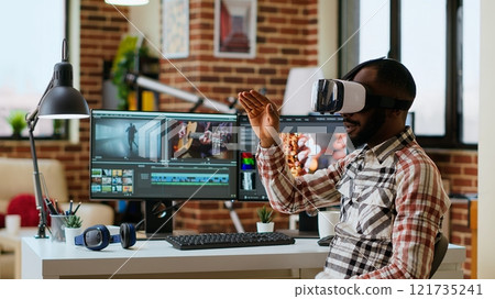 African american editor uses virtual reality glasses to do color grading, working with high tech vr headset and dual monitors at his home office. Filmmaker editing video clips. Camera B. African american editor uses virtual reality glasses to do color grading, working with high tech vr headset and dual monitors at his home office. Filmmaker editing video clips. Camera B. 121735241