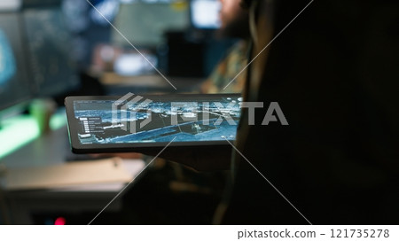 Army operative using tablet in command center housing operational missile defense system designed to intercept ballistic rockets. Close up of expert using tracking software on device, camera A 121735278