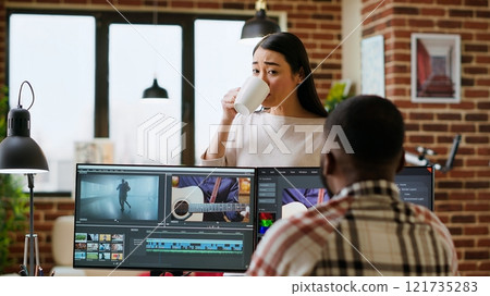 Creative team interracial partners collaborating on a video editing project, using high end video production software for color grading and mixing. Diverse couple uniting forces for work. Camera B. 121735283