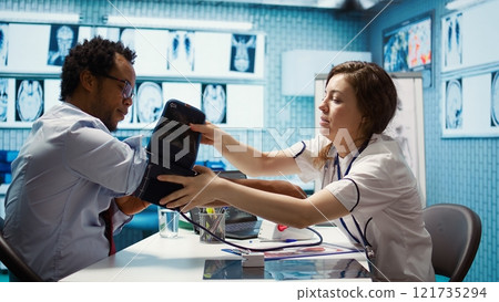 Physician doing a medical consultation with blood pressure monitor, taking pulse and heartbeat measurements for cardiac readings. Providing high quality control and healthcare services. Camera B. 121735294