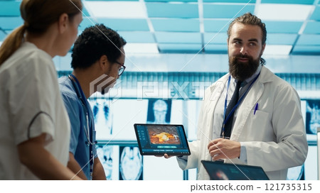 Neurology specialist examines magnetic resonance imaging brain scan with team during a meeting, looking at tomography for accurate neuroscience diagnosis. Diverse team of doctors. Camera A. 121735315