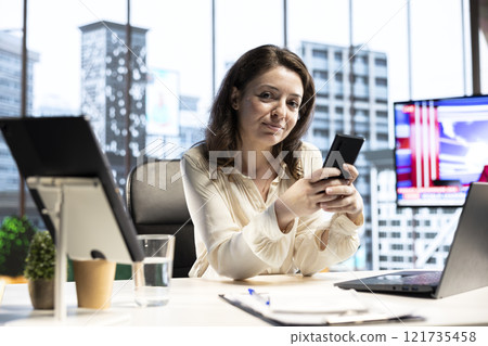 Portrait of female entrepreneur checking her personal phone messages in her CEO office, determined boss lady with a success story. Woman director feeling confident in business industry. Portrait of female entrepreneur checking her personal phone messages in her CEO office, determined boss lady with a success story. Woman director feeling confident in business industry. 121735458