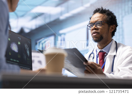 Male physician doing an x ray diagnostics scan interpretation during check up visit, discussing about recovery treatment in cabinet. Doctor examining radiography test results for a patient. 121735471