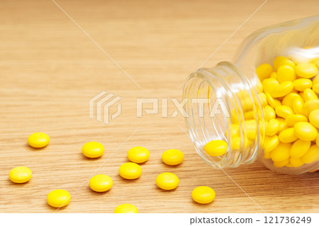 黃色藥丸從掉落的透明瓶子中散落 121736249